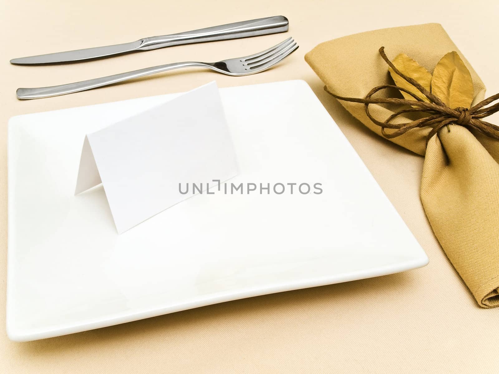 decorated table serving with golden bay leaves in serviette and cord near plate, knife and fork at beige 