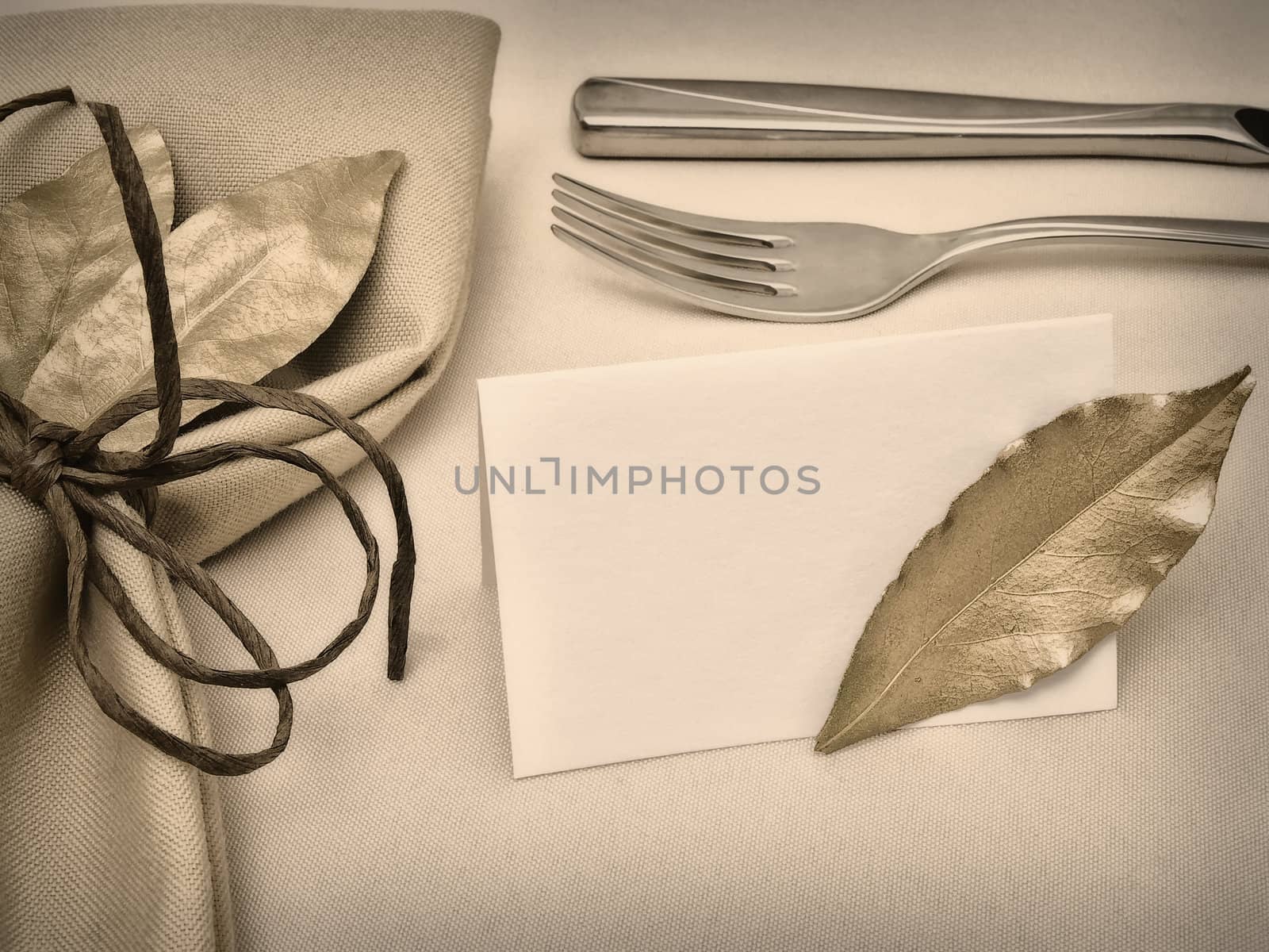 decorated table serving with golden bay leaves in serviette and cord near knife, fork and guest card at beige 