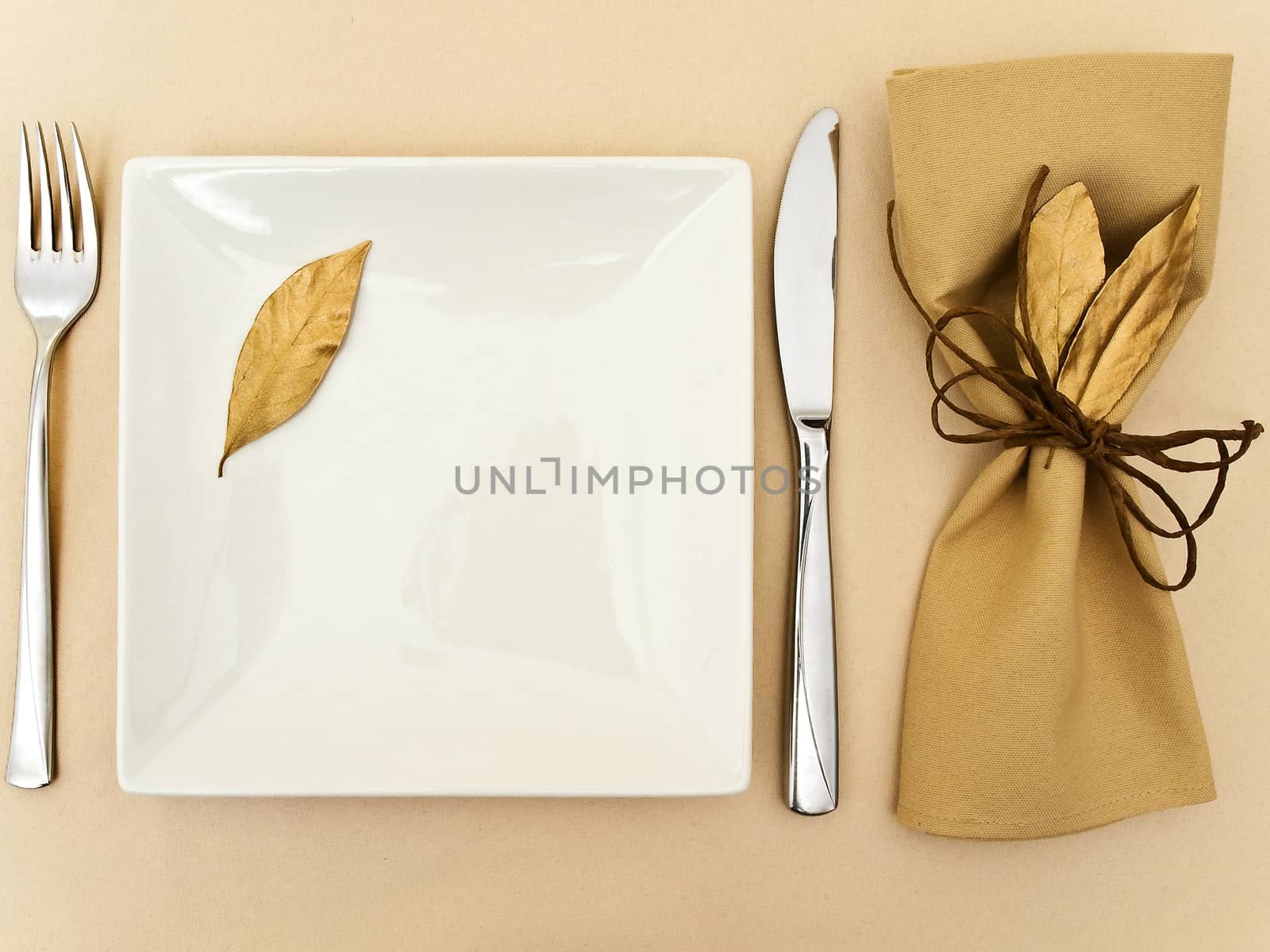 original table serving with golden bay leaves in serviette and cord near plate, knife and fork at beige 