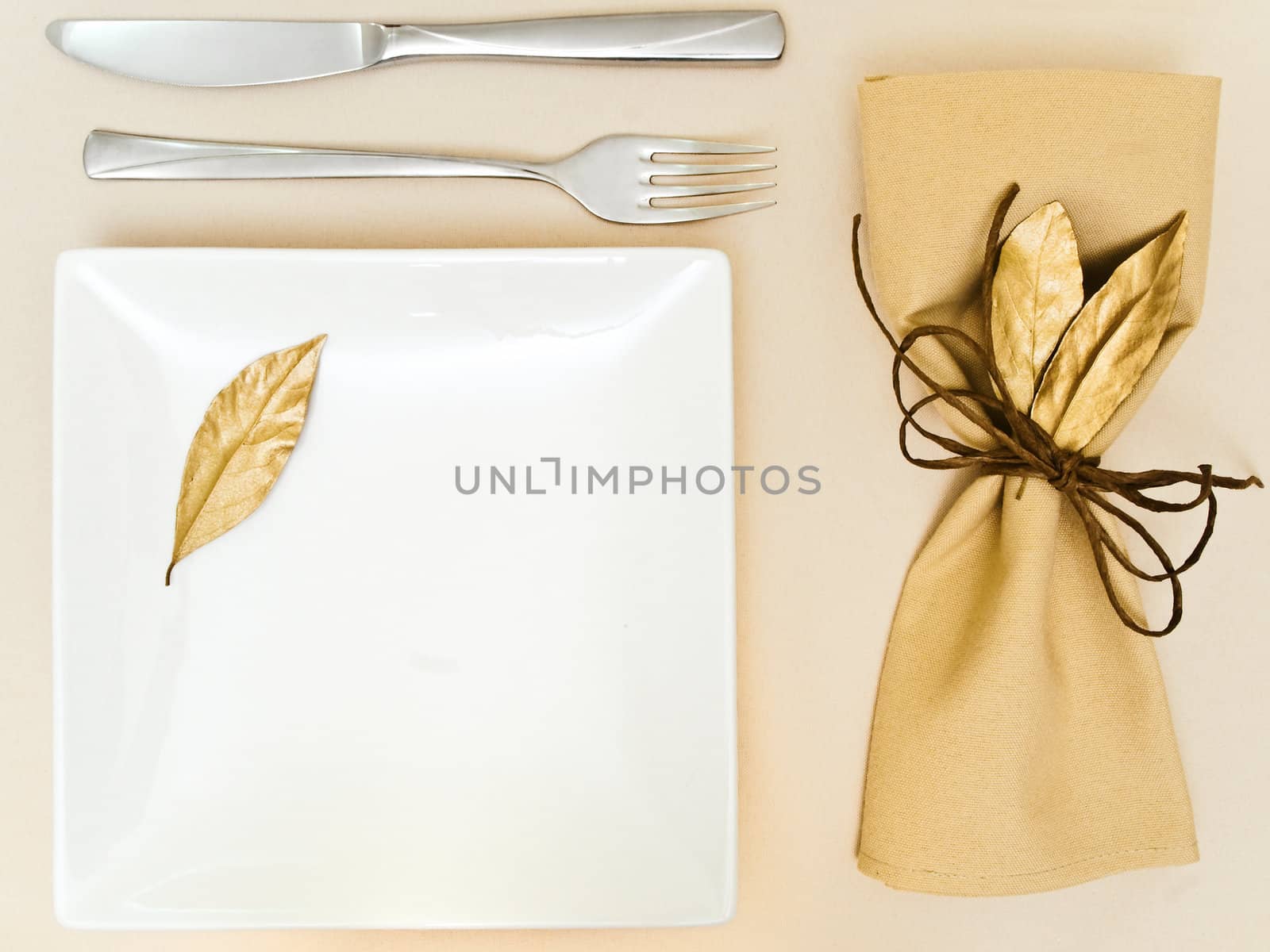 table serving with golden bay leaves in serviette and cord near plate, knife and fork at beige 