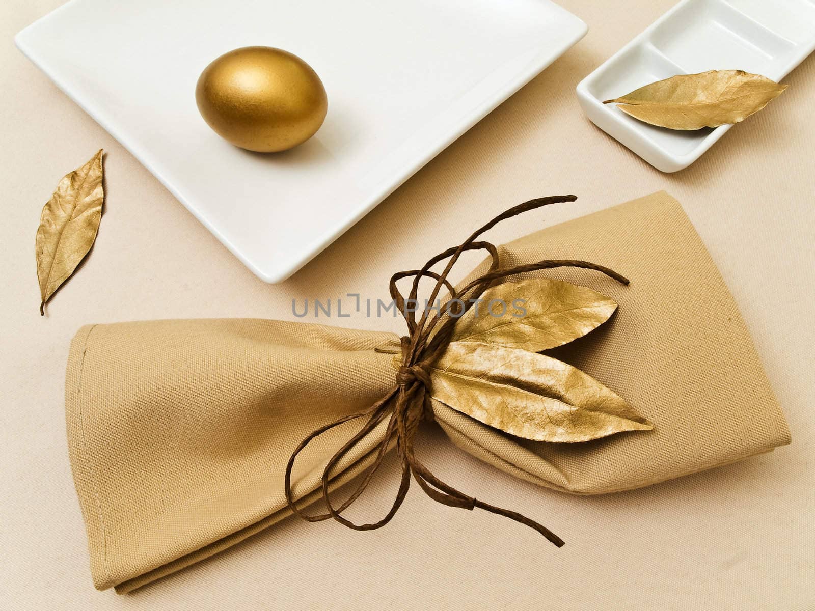 original table serving with golden bay leaves in serviette and cord near plate at beige  
