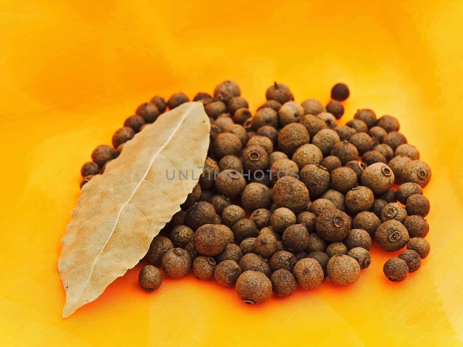 allspice and bay leaf over orange textile background