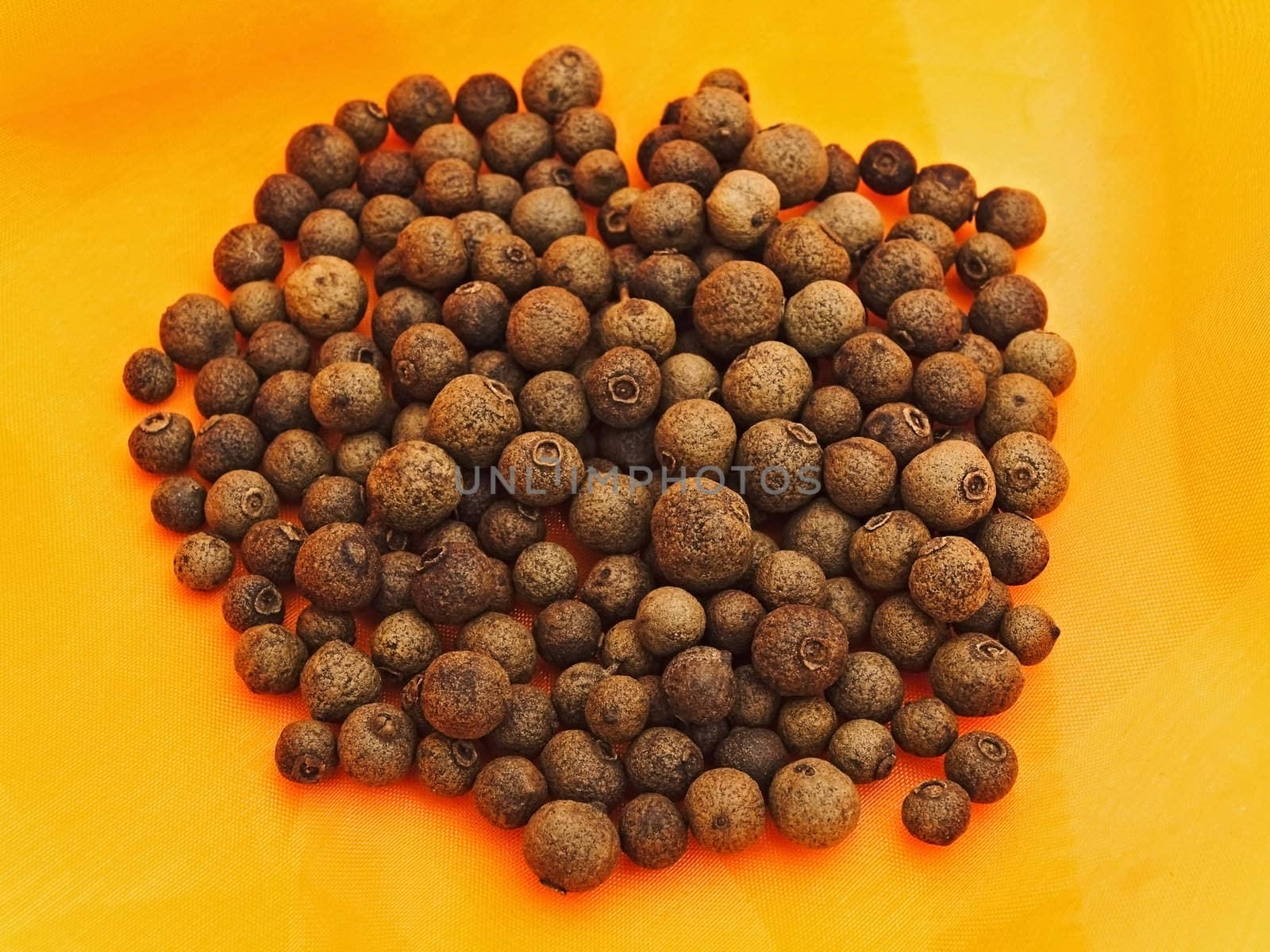 heap of allspice  over orange textile background