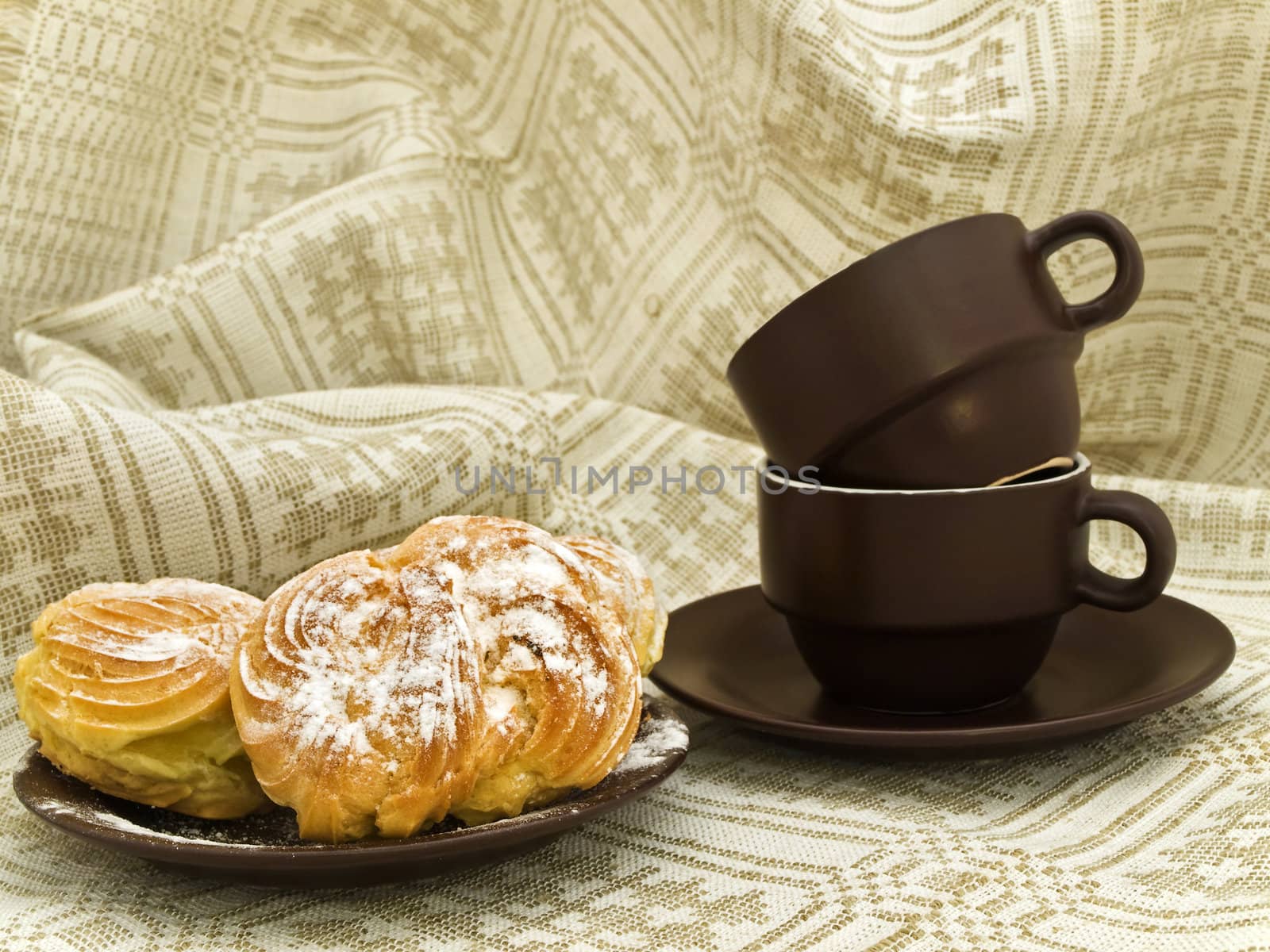 Two tasty buns with sugar powder and brown coffee cups against the linen background 