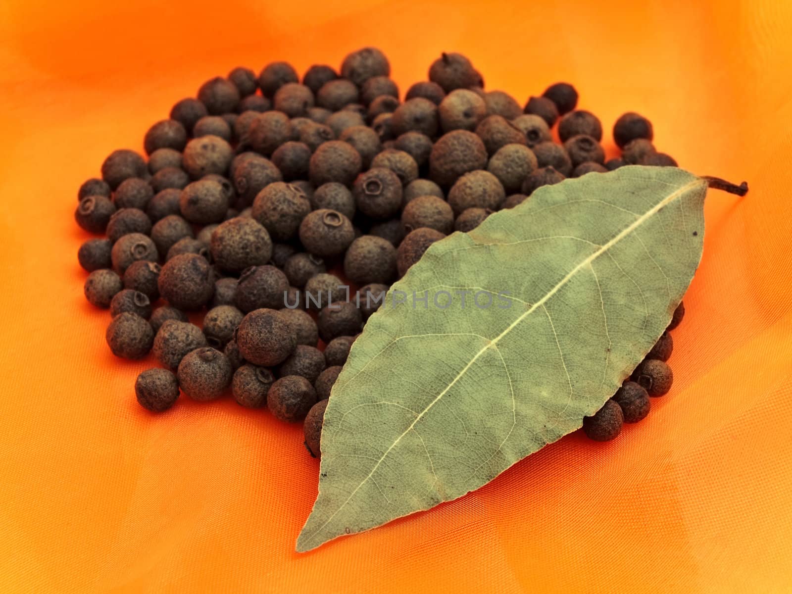 Photo of organic black pepper stack and single bay leaf at orange textile