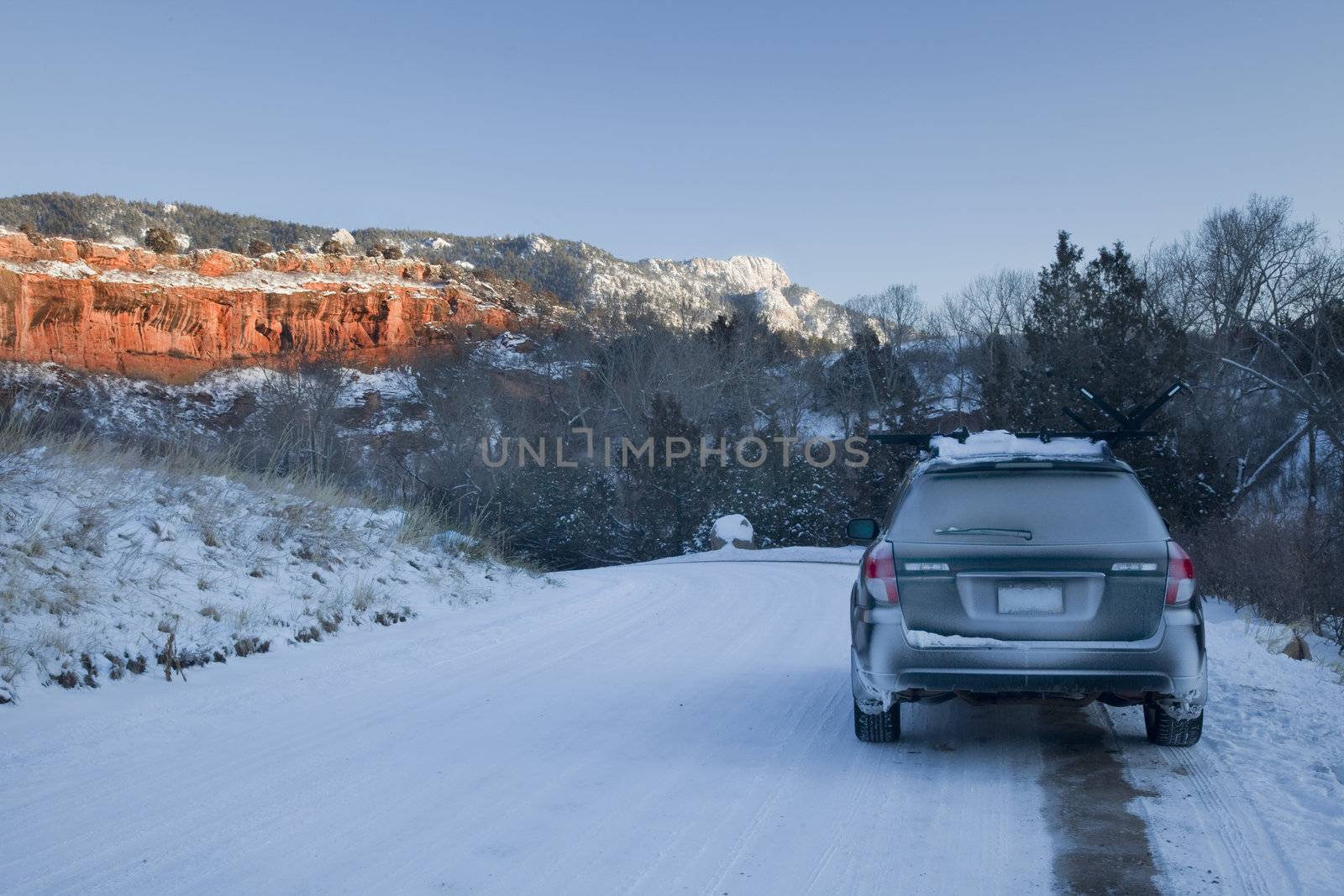 passenger car and snow covered road in Colorado backcountry with red sandstone cliffs and Horsetooth Rock near Fort Collins in sunset light