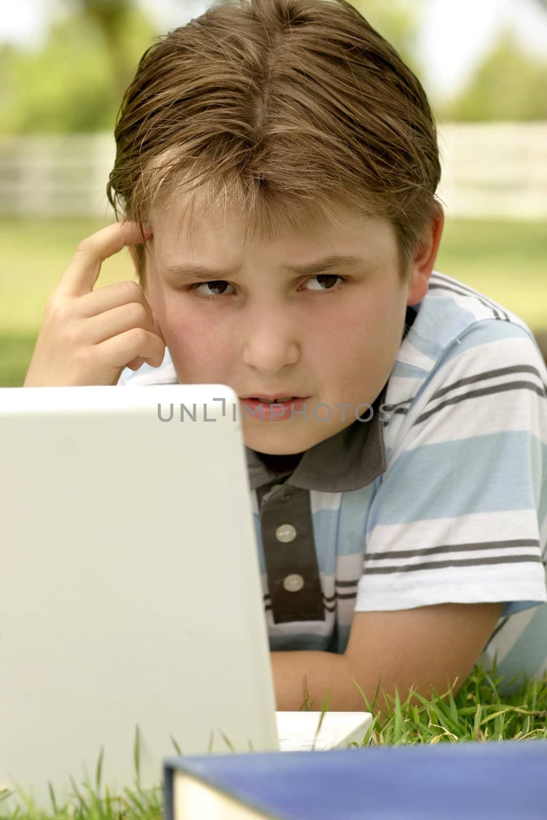 A puzzled looking boy working on computer outdoors.
