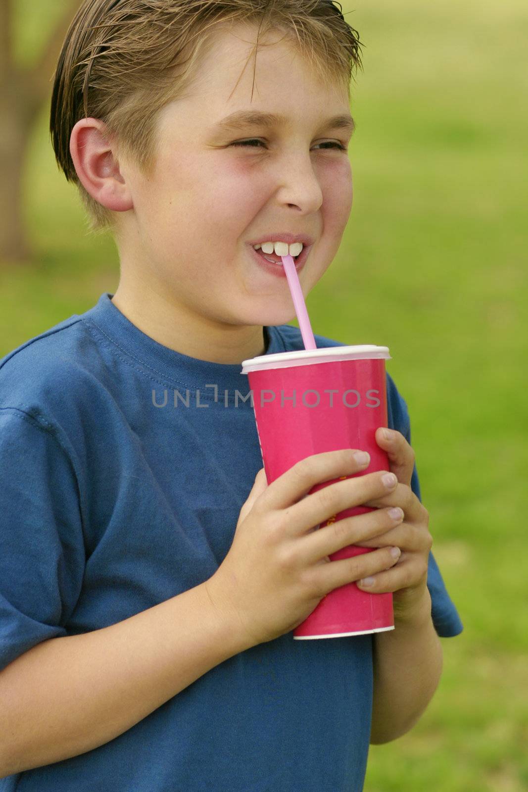 Boy holding a  strawberry milkshake in a pink disposable cup in a park
