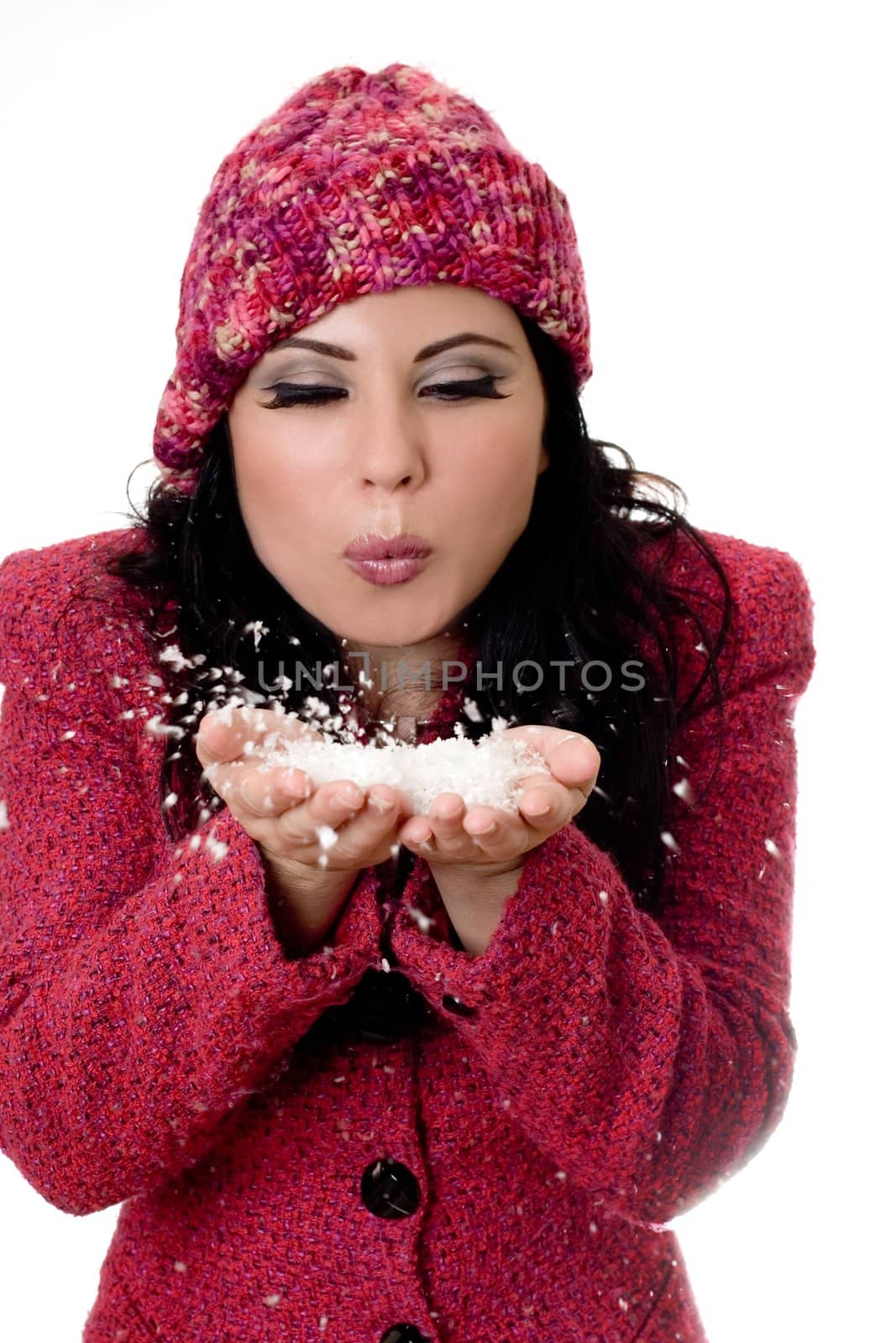 Winter woman wearing wool boucle jacket and woolen beanie blowing soft white flakes from palms of hands.