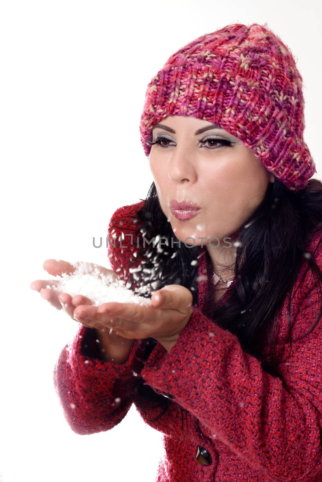 Female wearing wool boucle jacket and woollen beanie gently blowing soft white flakes.