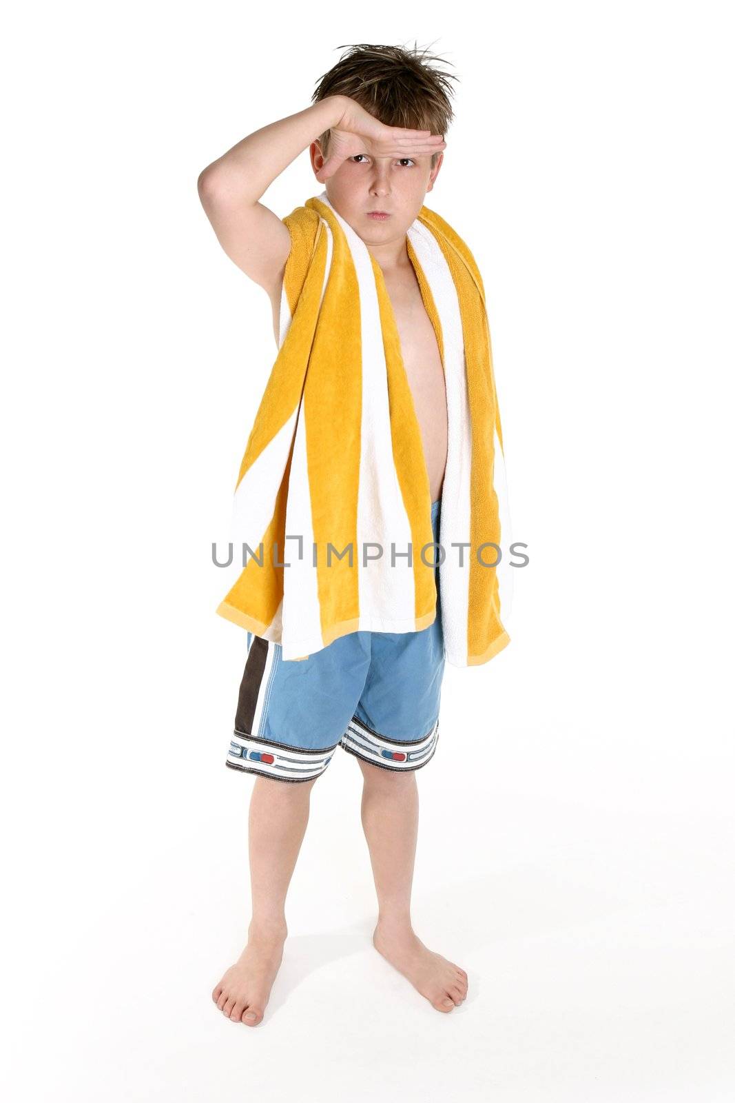 Boy in board shorts and beach towel slung over shoulder looks out to the surf.