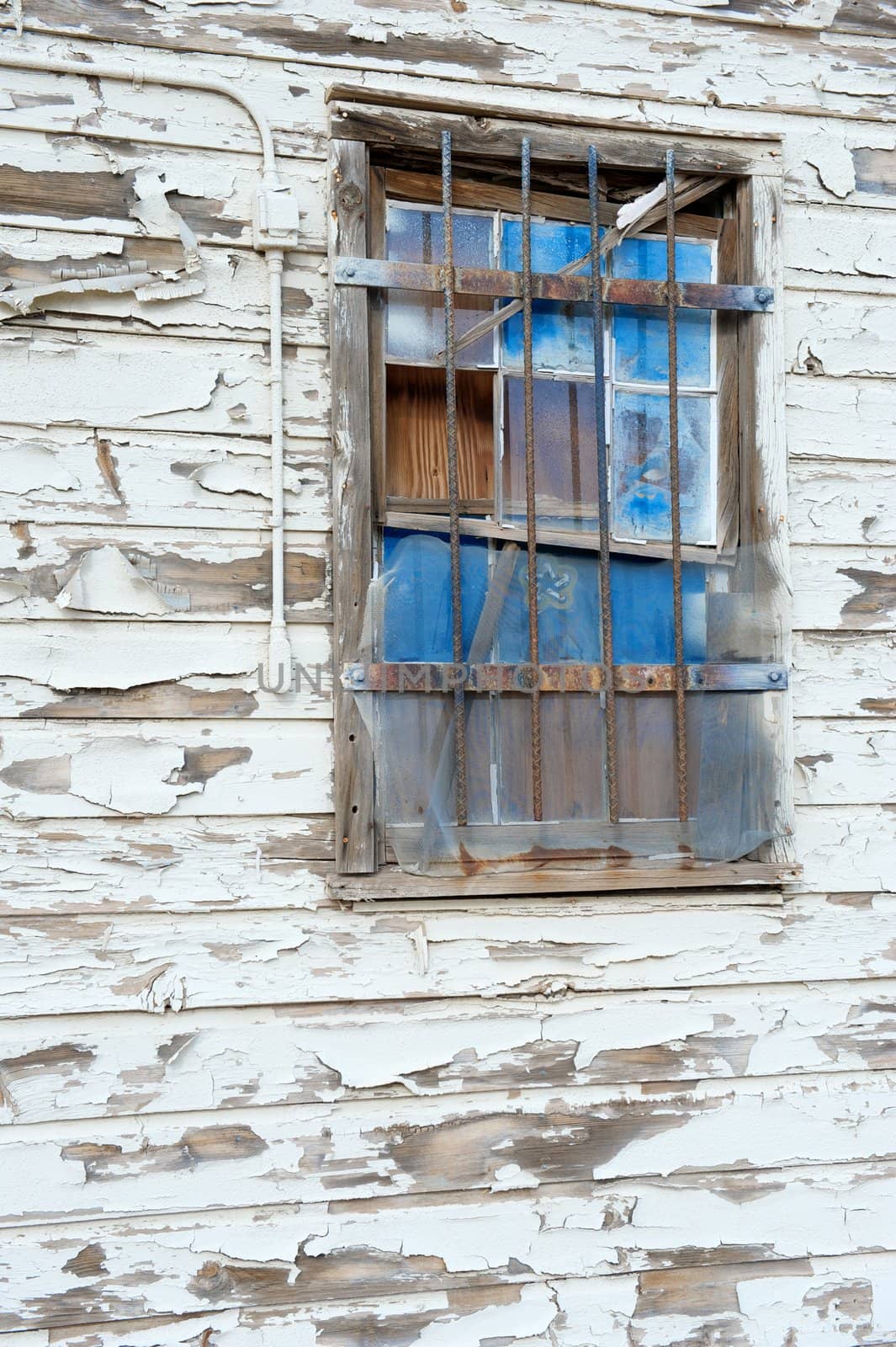 A boarded up window with broken blue panes of glass that has bars on it
