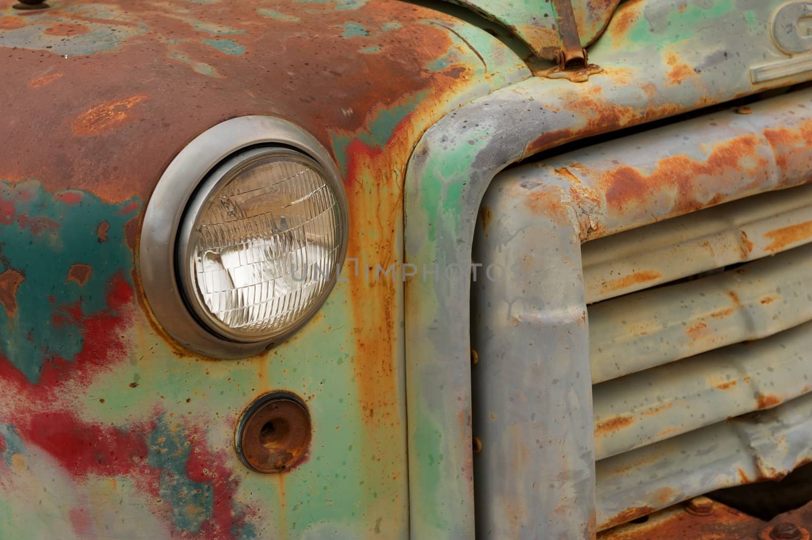 A green and red painted rusty front grill of an antique truck with glass headlight