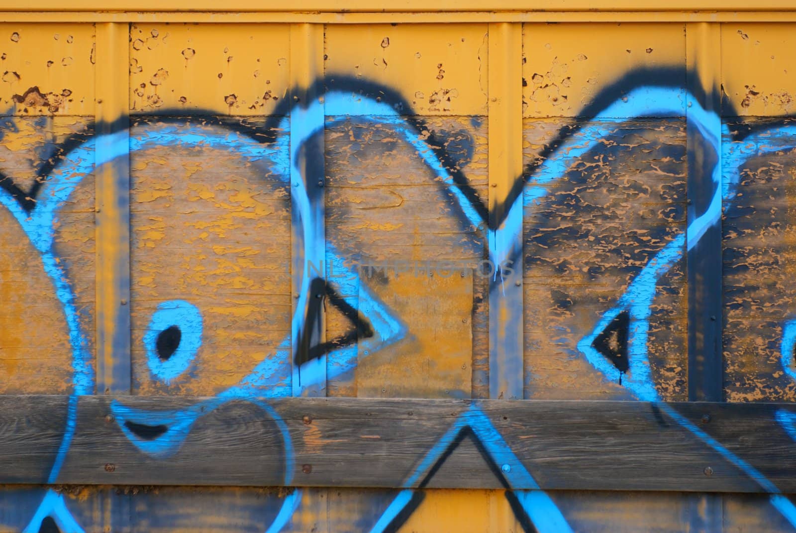 A tagger spraypainted some letters on the side wall of a yellow train boxcar