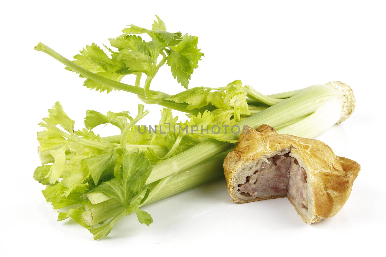 Contradiction between healthy food and junk food using celery and pork pie on a reflective white background 