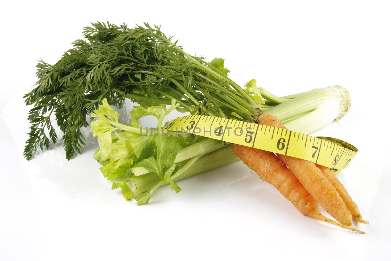 Fresh bunch of orange carrots with green leafs and celery with a yellow tape measure on a reflective white background