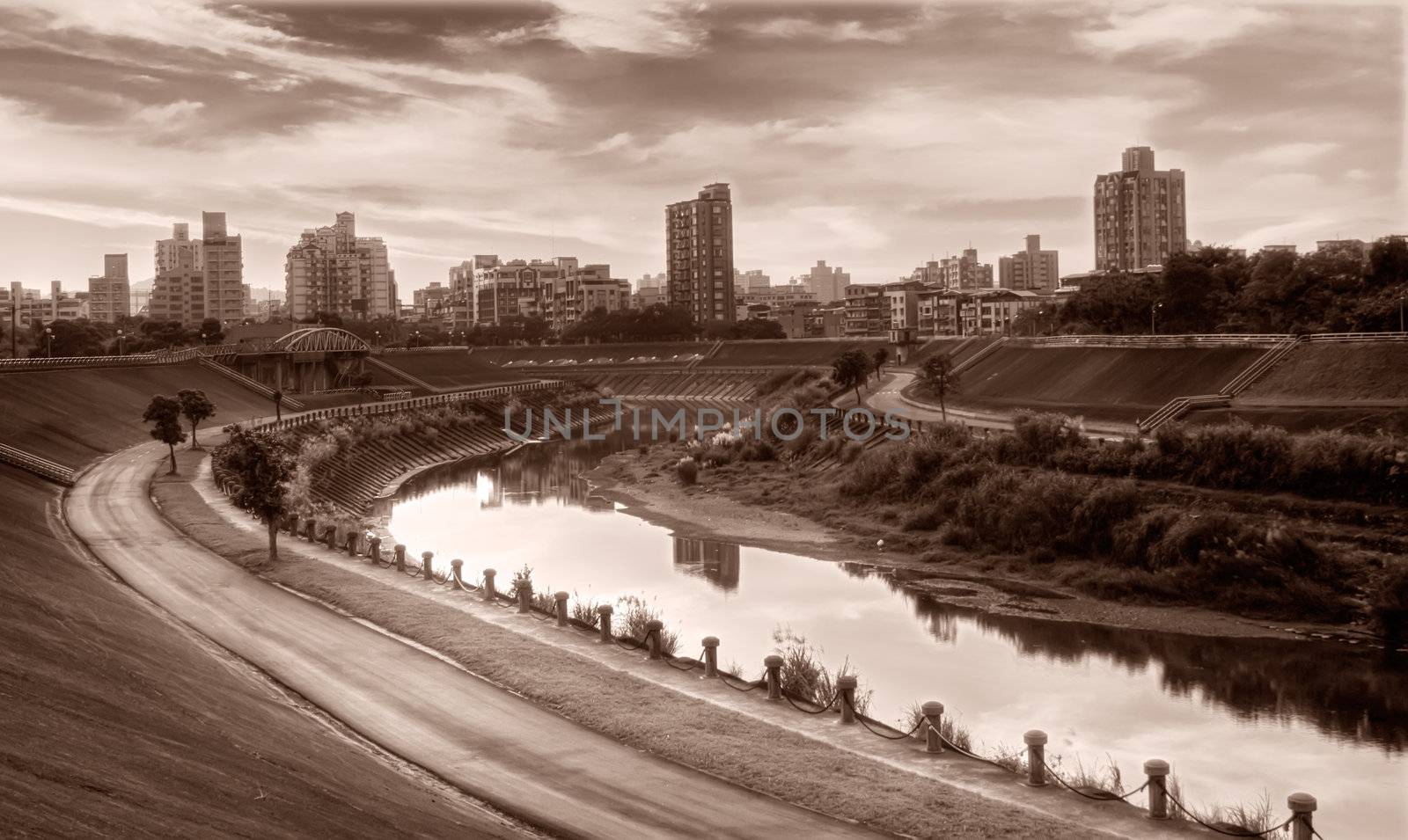 Apartments and park near river in the modern city sunset evening.