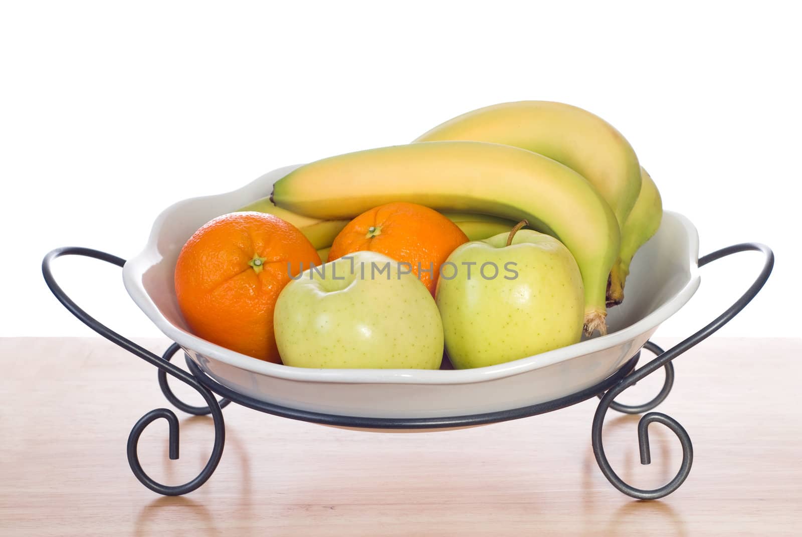 Assorted fresh fruit including bananas, oranges and apples, sitting in a bowl and shot on a wooden table