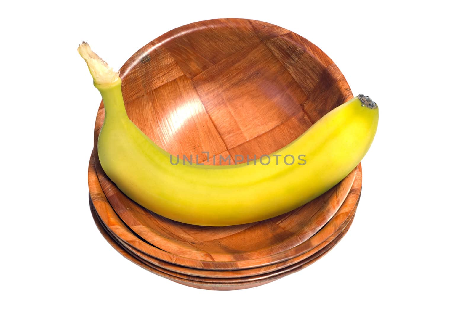 A fresh banana sitting in a wooden bowl, at the top of a stack of bowls, isolated against a white background