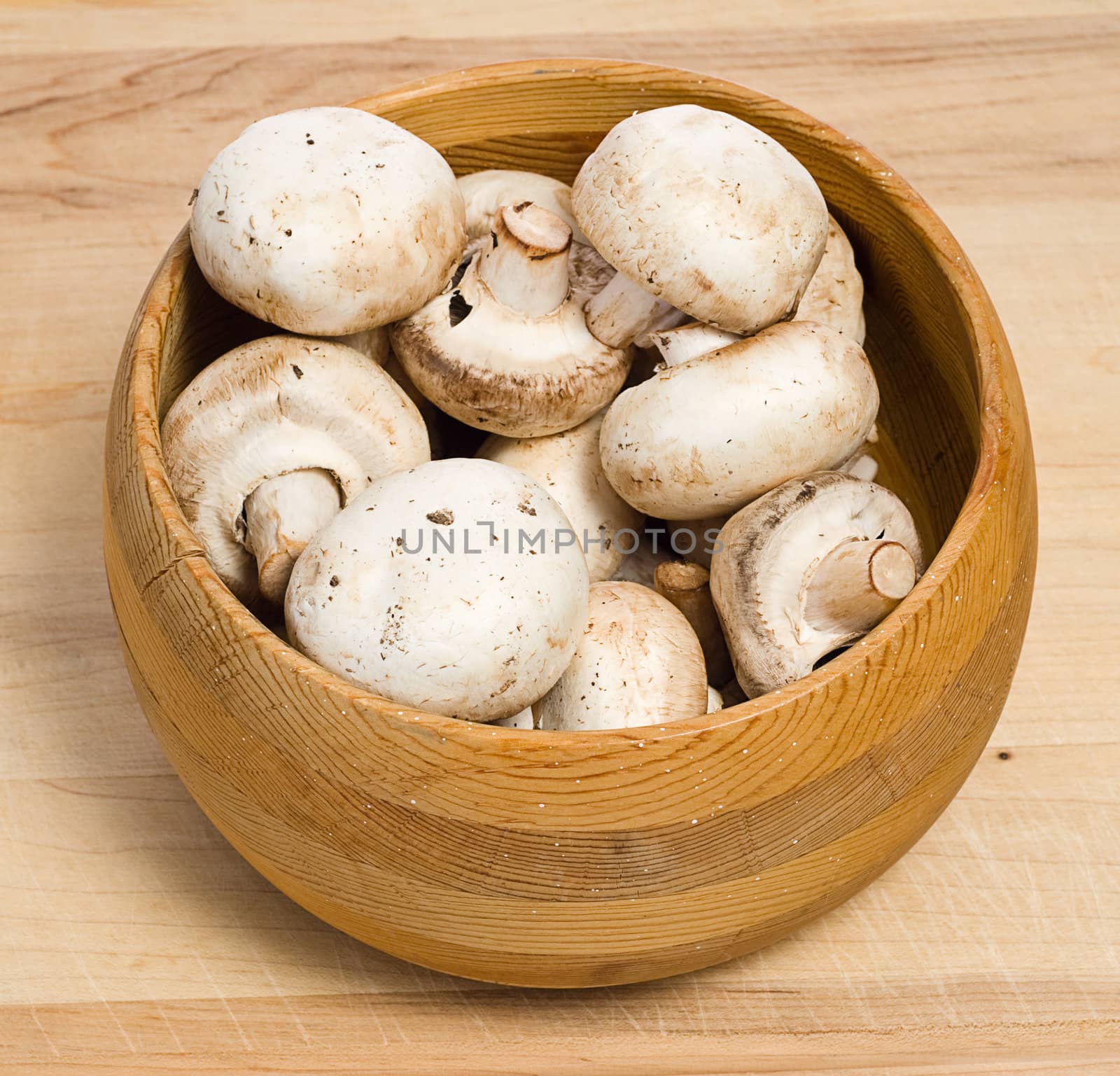 A bowl of white mushrooms, shot on a wooden cutting board