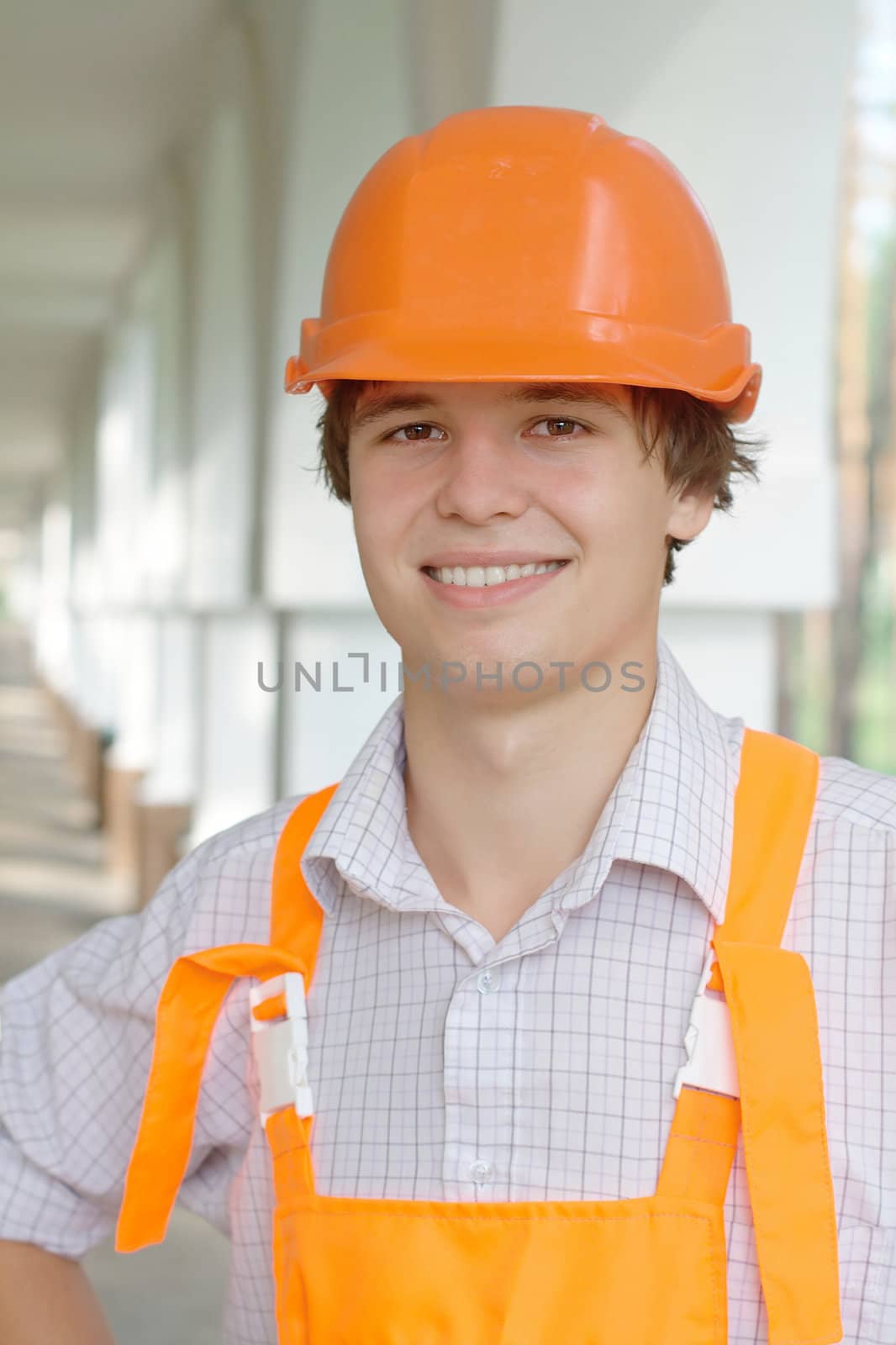 Close-up portrait of a smiling young worker in an orange hardhat outdoors