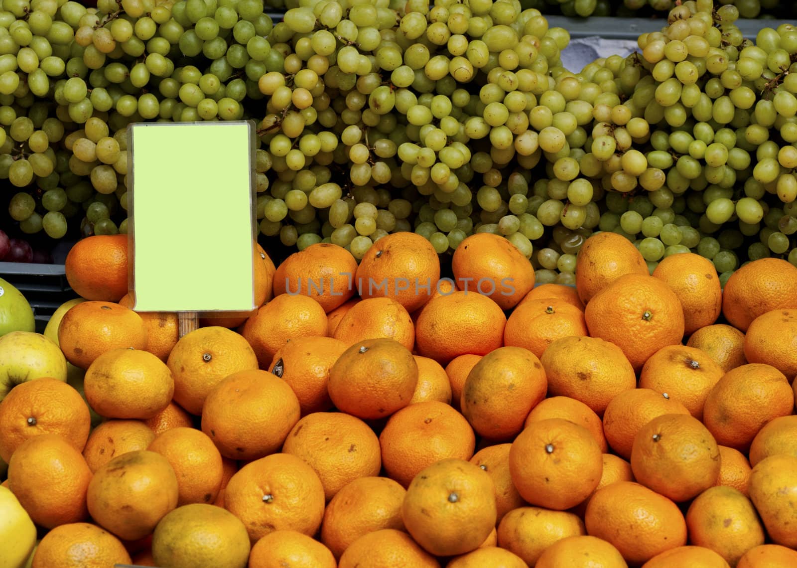 green grapes and oranges with a sign at a market