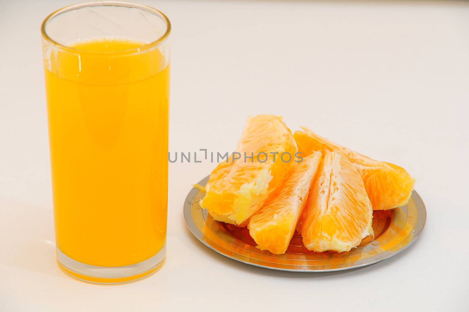 Orange juice in a glass and orange wedges on the saucer.