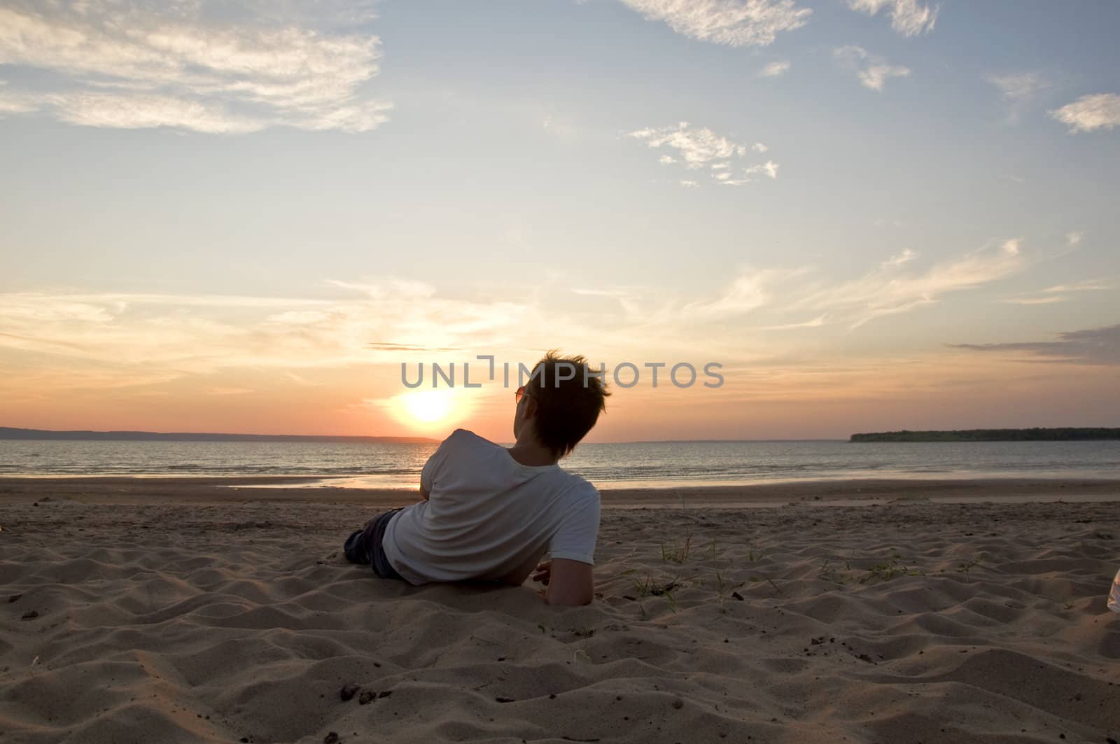 Young man lying on the beach back to the camera and watching the sunset. Summer Landscape.