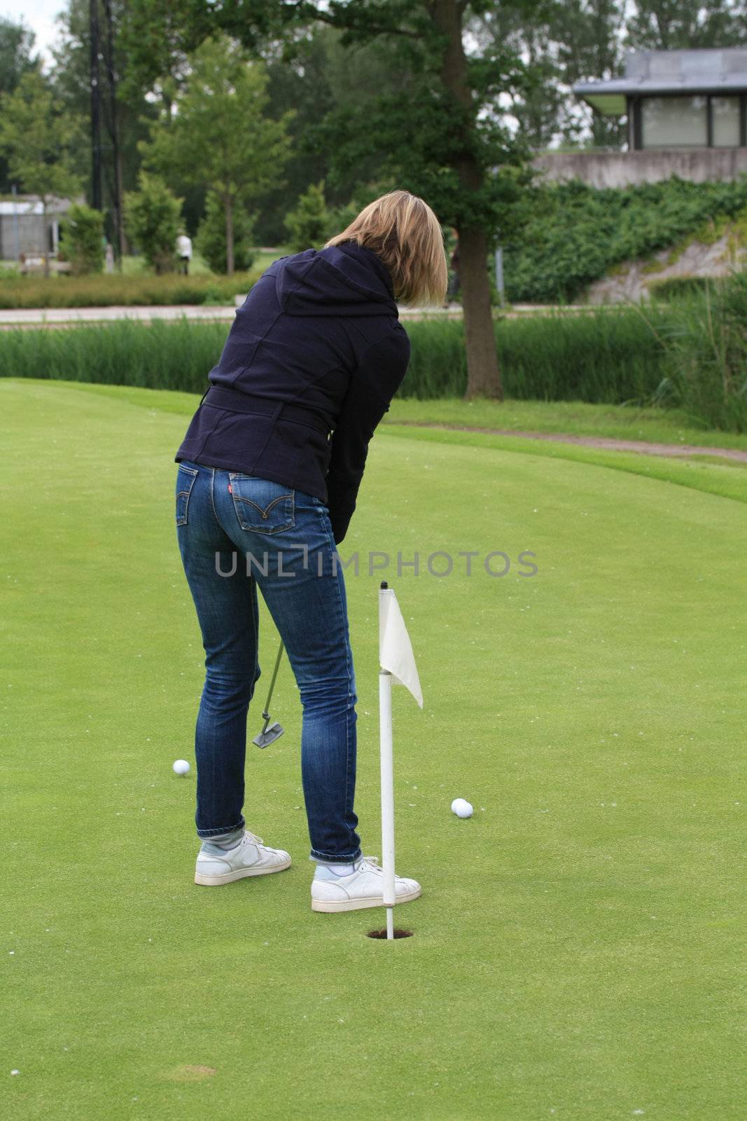 woman practising golf on chipping green by studioportosabbia