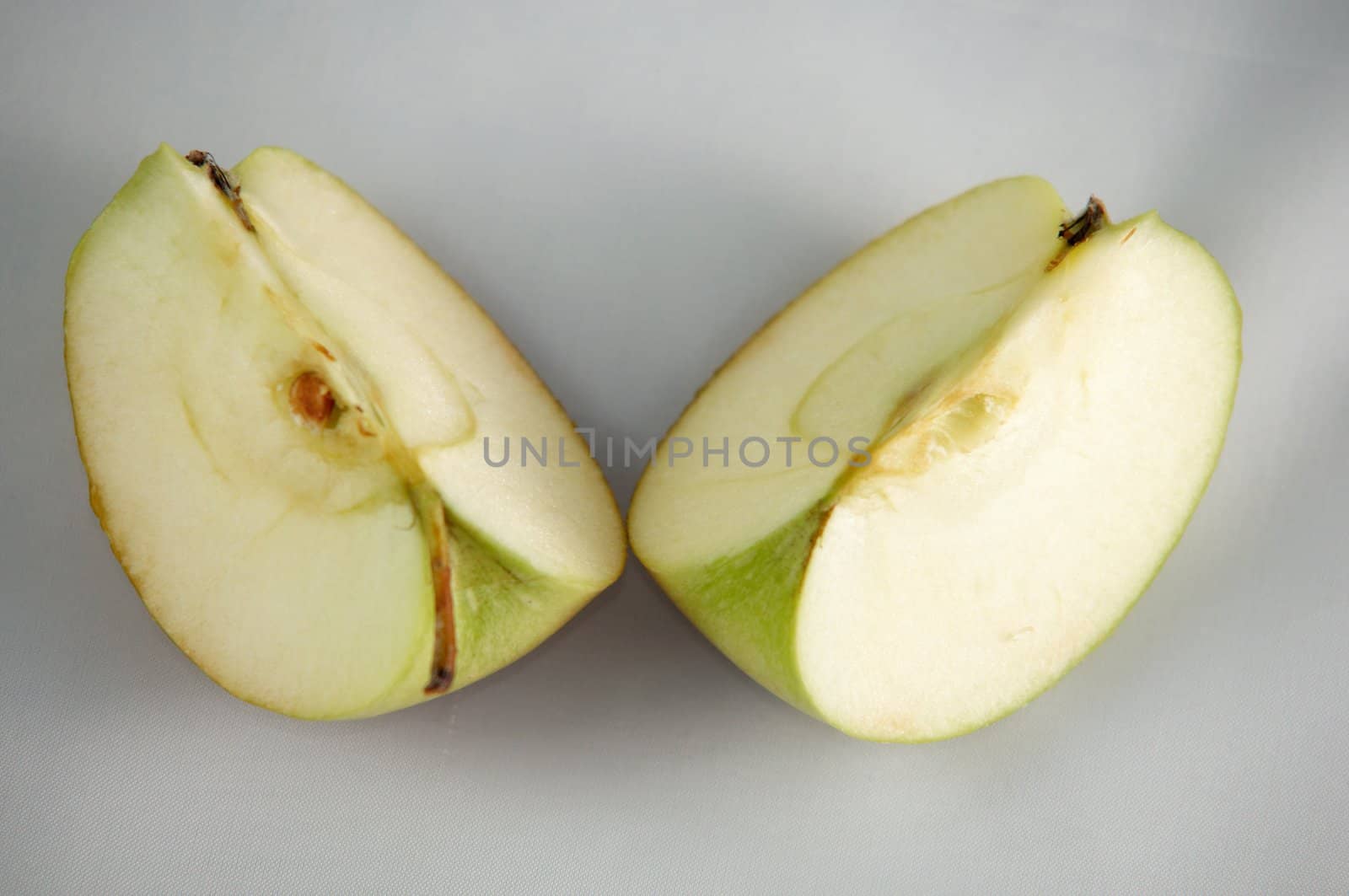 Two quarters of green apple on a white surface.