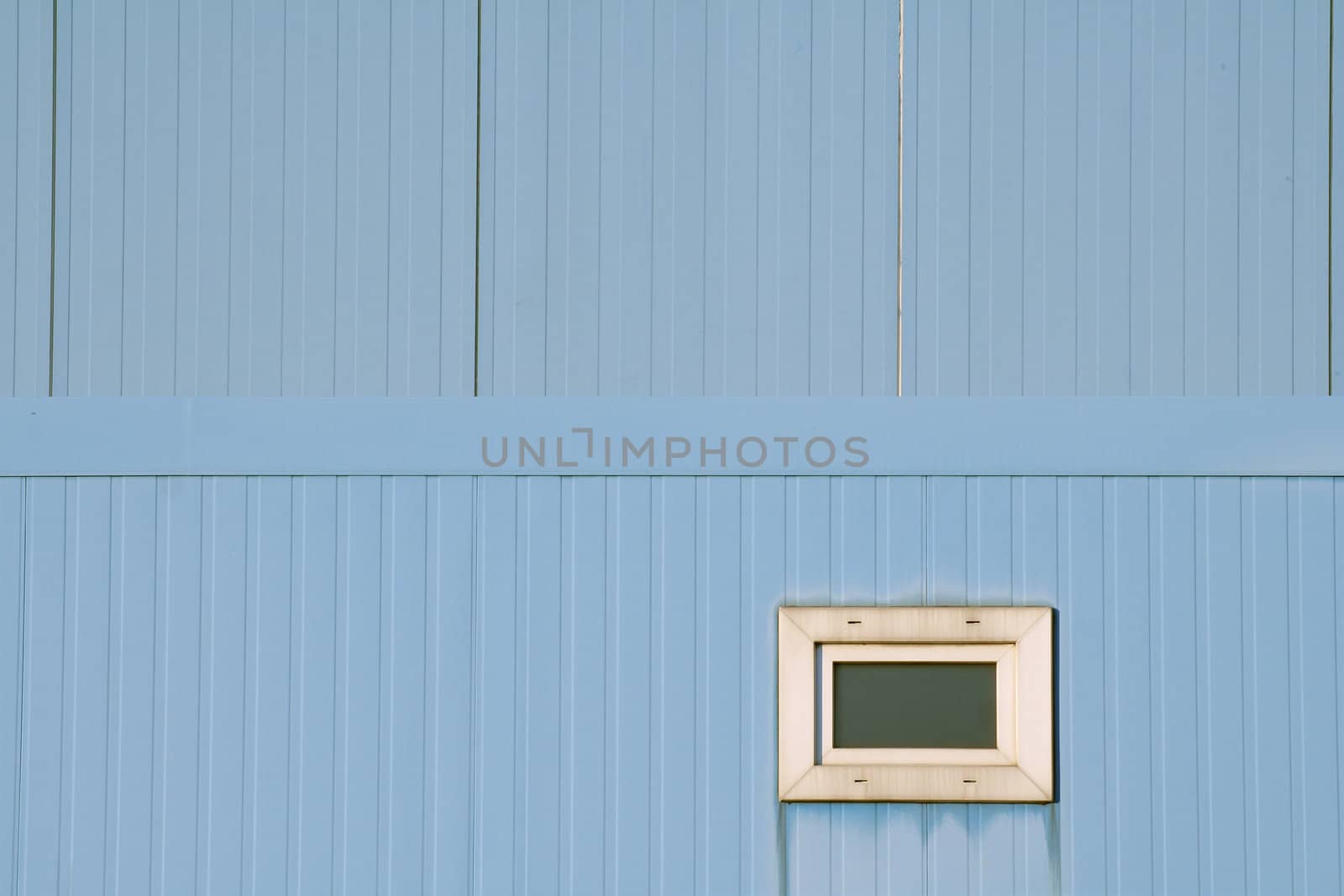 Very small window in blue industrial facade. Focus on lower half, which is the foreground. Geometrical abstract.