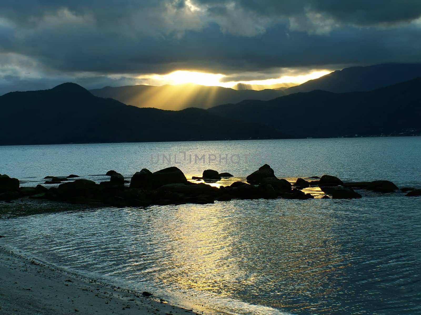 Yellow sun rays through clouds, passing over the mountains and making a nice reflection on the sea surface