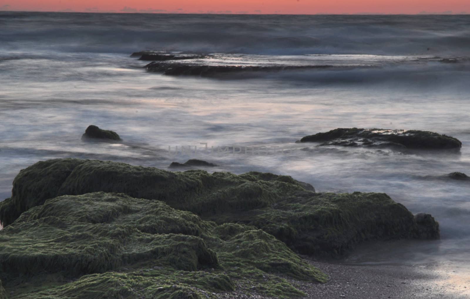 Sunset at Sea. Small waves. Stones overgrown with moss.