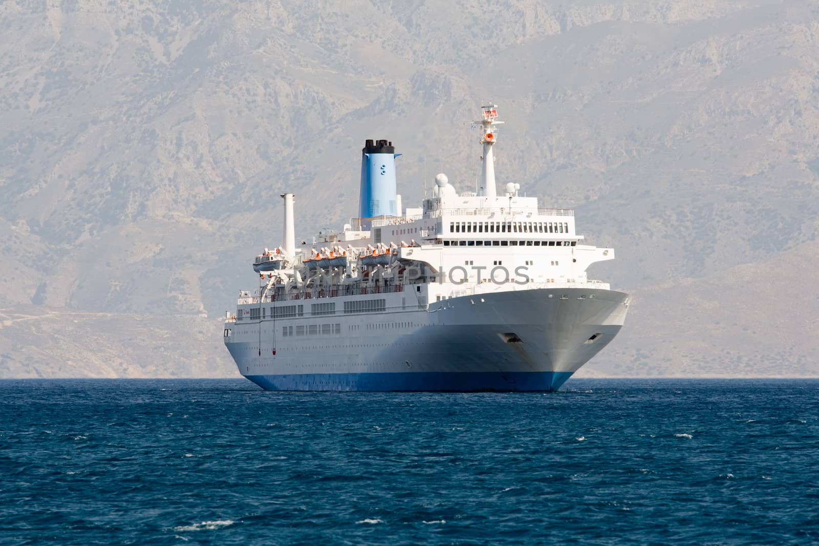 Tourist white cruise sea liner is sailing in rocky bay on the mountain background