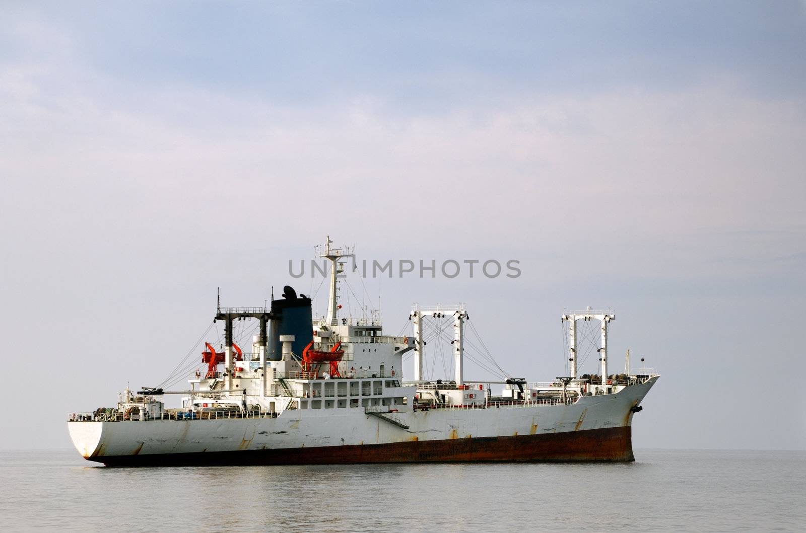 Image shows a white merchant ship floating over calm waters
