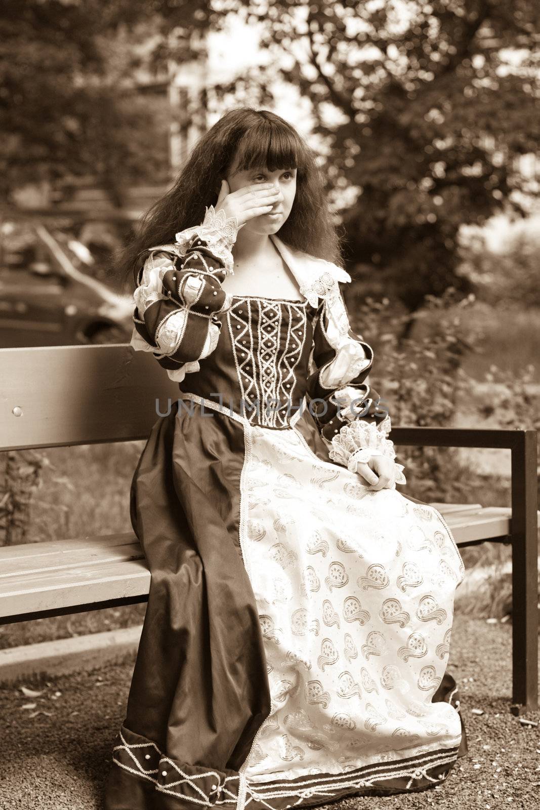 A girl in medieval dress sitting on a bench 
