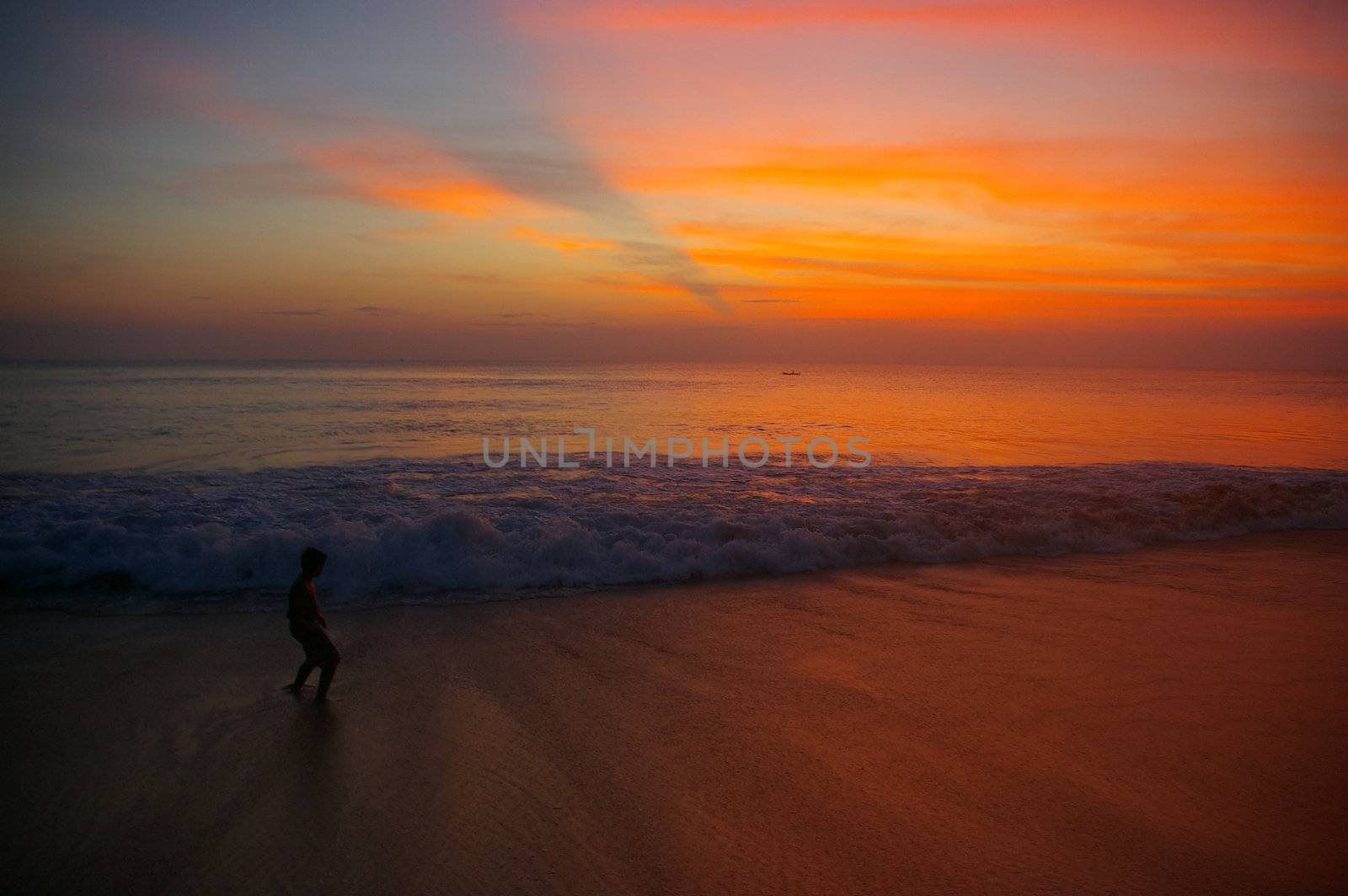Boy on a beach at sunset with waves rolling towards him. Dreamland beach, Bali, Indonesia.