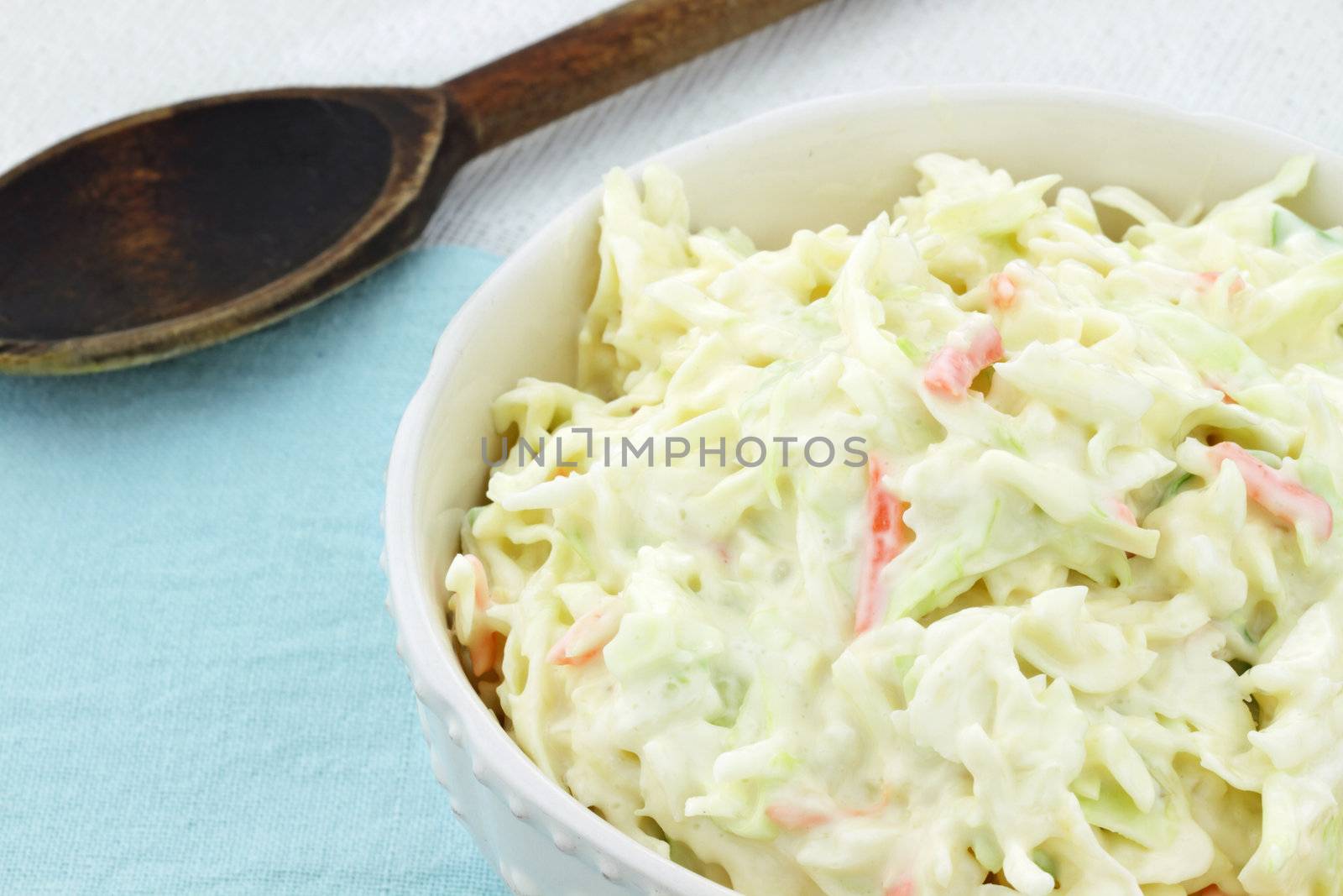 Homemade coleslaw in a white bowl with an old wooden spoon in the background.