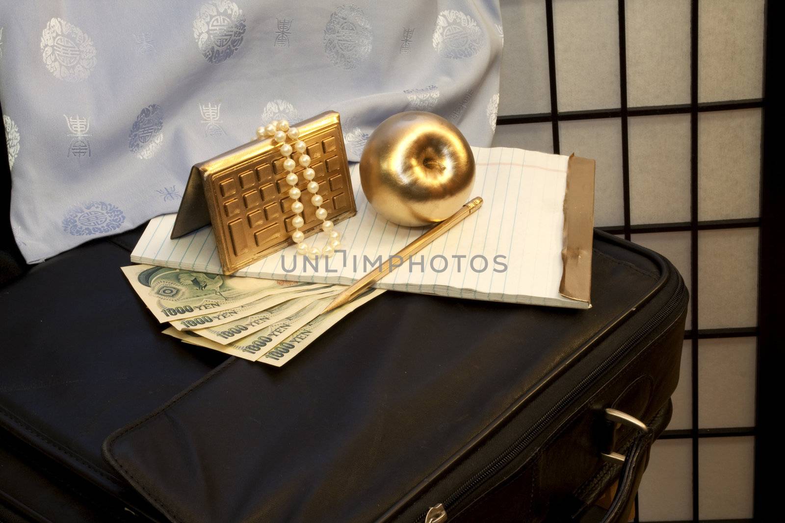 Blue silk and pearls contrast with the yen and black briefcase to suggest femininity in a male business environment; golden calculator and golden apple enhance with suggestions of opportunity and success; 