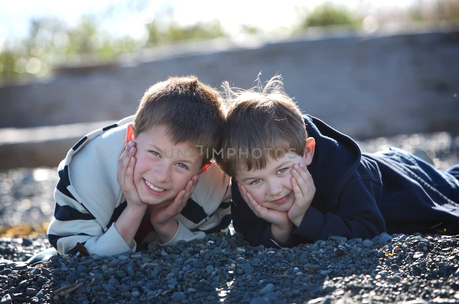 two cute boys lying on a rocky beach smilling at the camera
