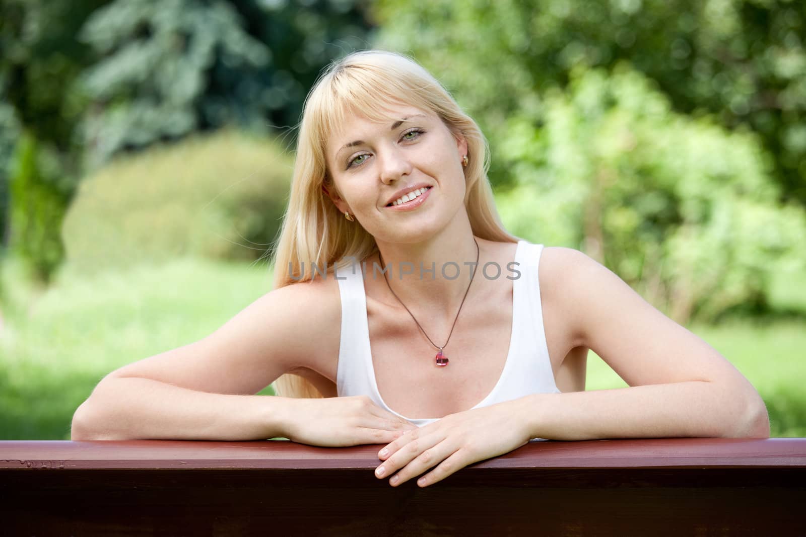 Young Smiling optimistic cheerful blond girl 20-29 sits on the bench in summer park