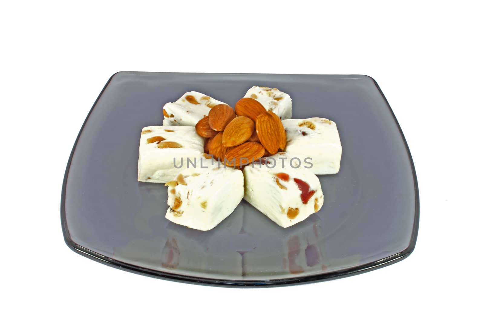Delicious nougat with almonds on black glass plate, isolated on white