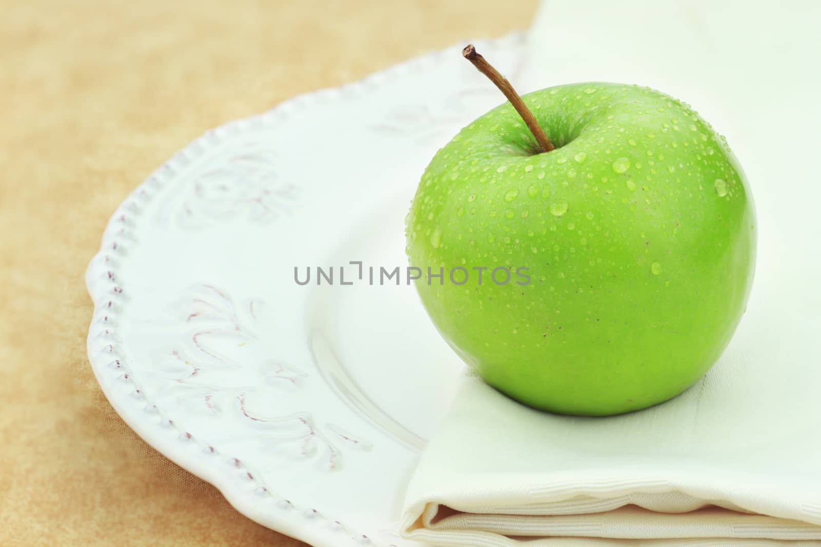 Green apple with water droplets on a dinner plate.