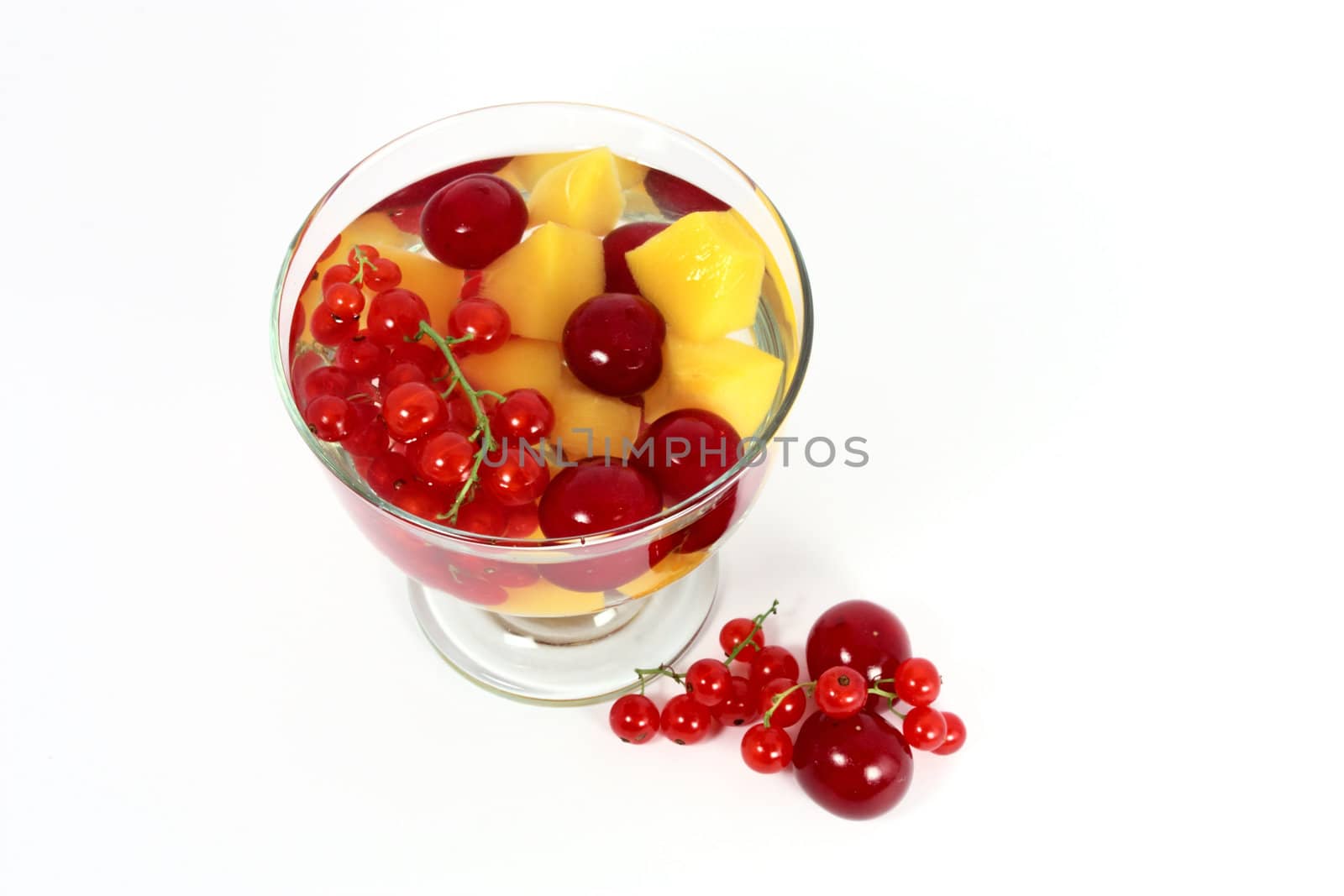 Peach compote with fresh red currants and sour cherries in glass isolated on white