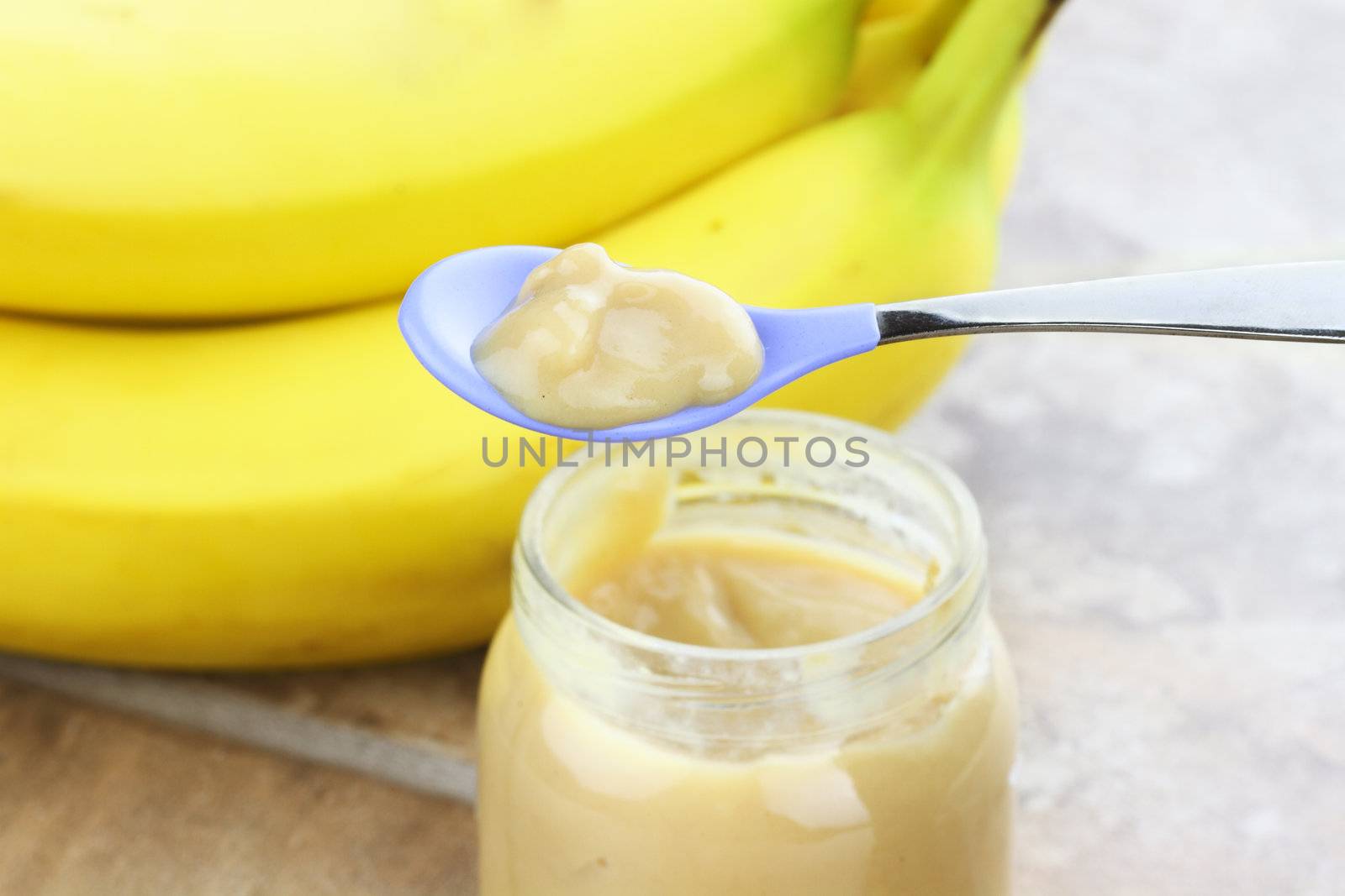 Pureed baby food from a jar with fresh bananas in background.