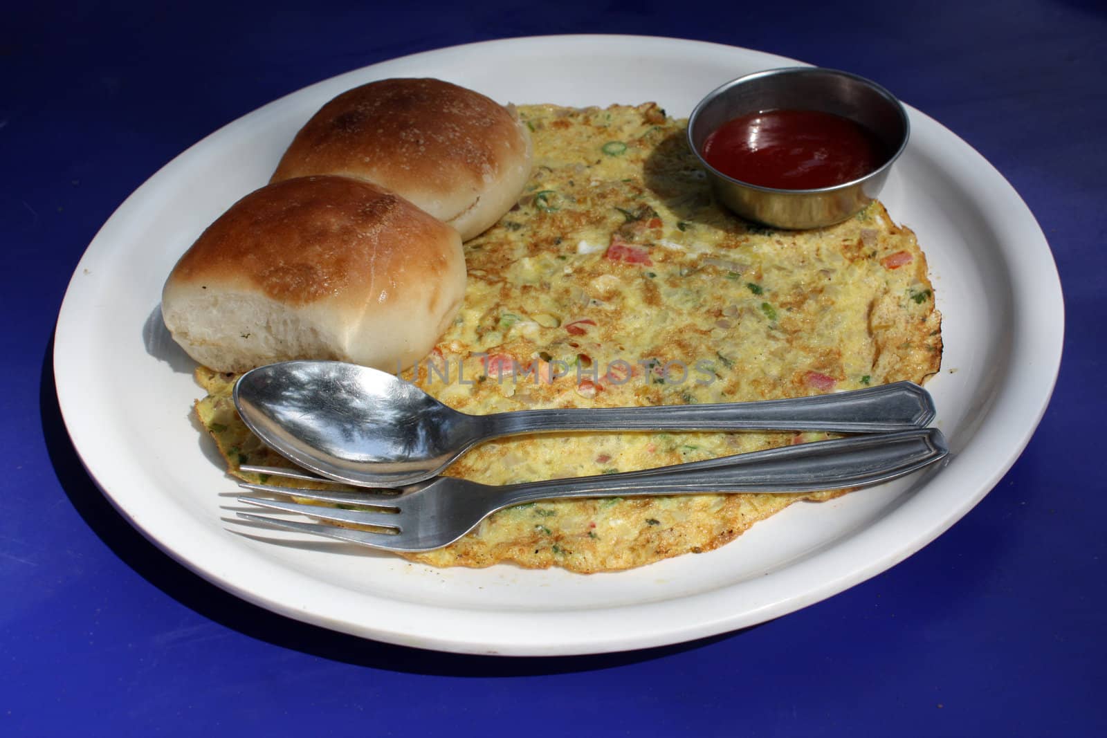 A plate of breakfast containing egg omelette, bread & sauce, in a restaurant on a blue table.