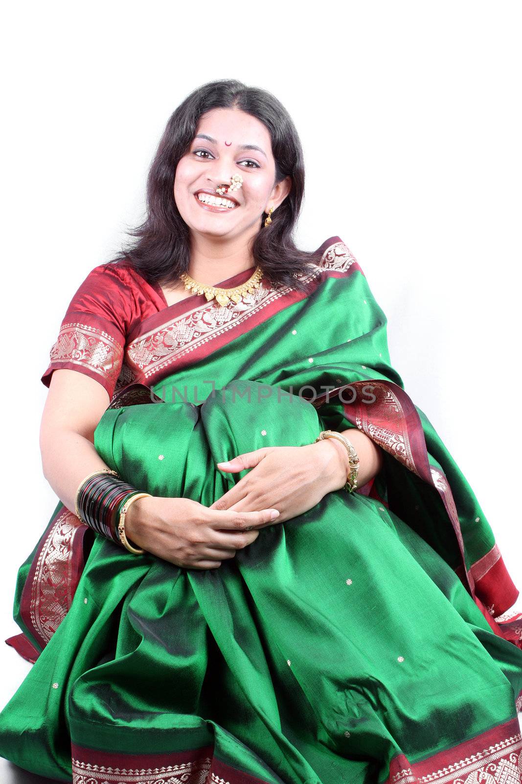 A happy Indian woman wearing a green sari, sitting on a white background.