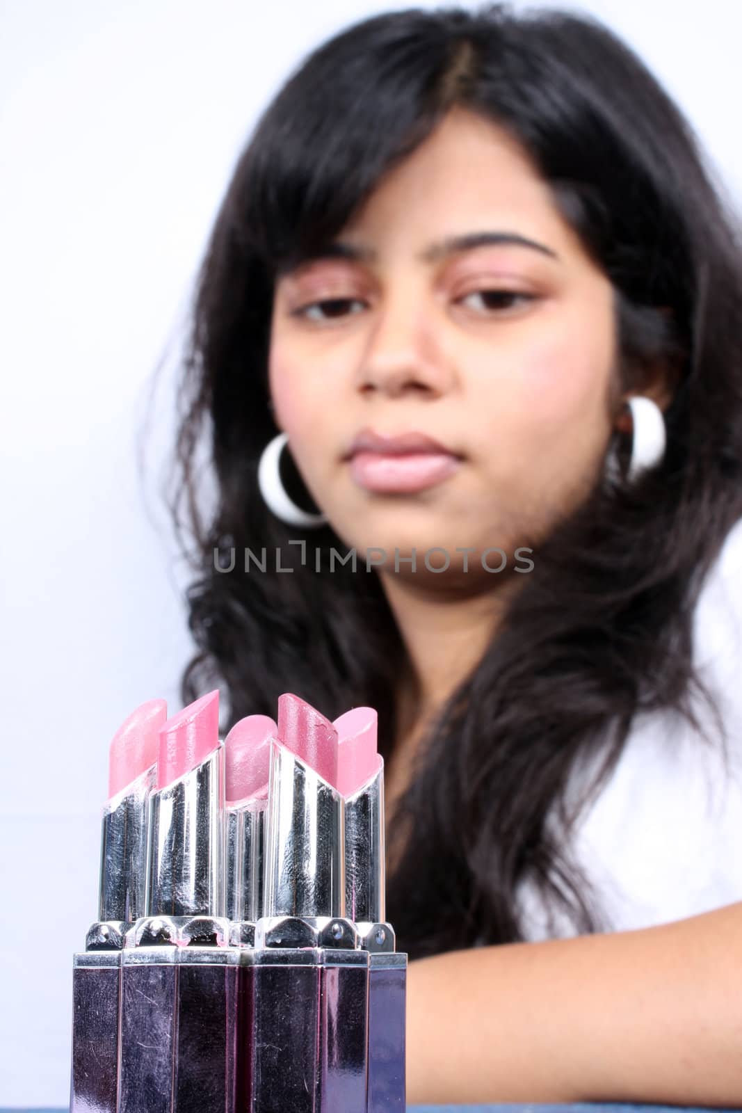 A metaphorical cosmetic background with a view of variety of lipsticks for choice in front of a teenager.