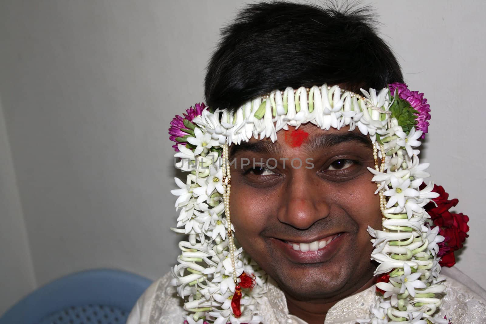 A portrait of a jovial Indian groom in traditional attire of flowers and garlands.
