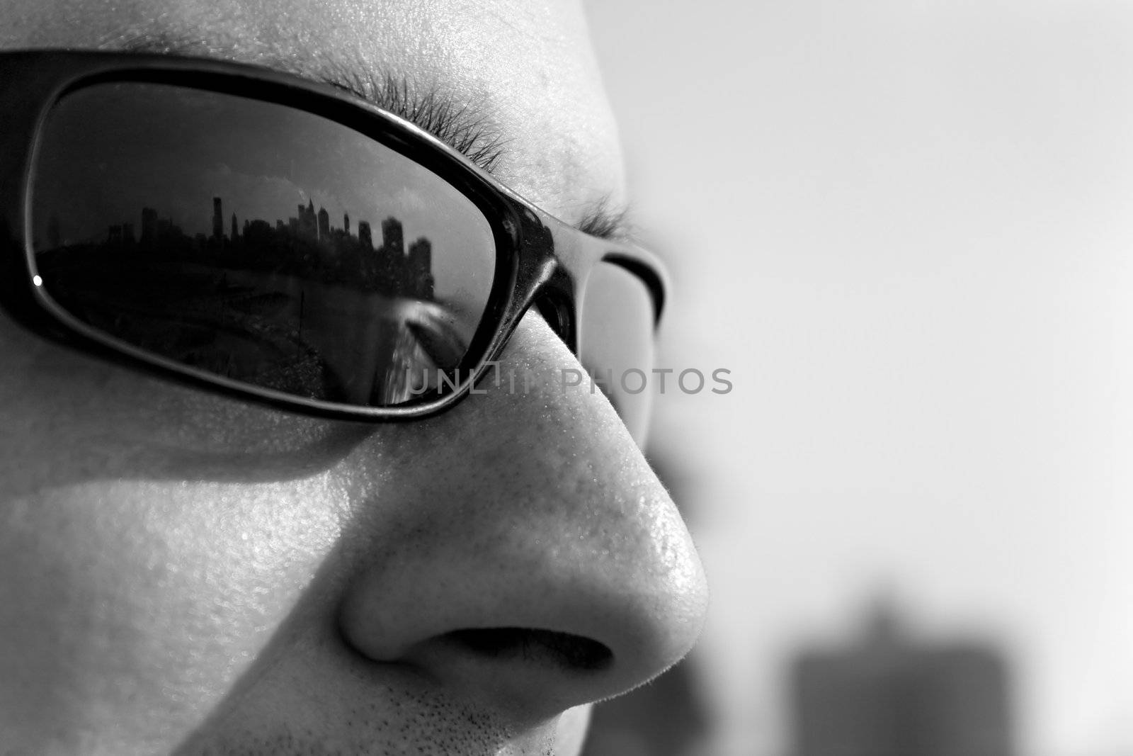 Close up of a man wearing sunglasses with the New York City skyline reflecting in the lens. Shallow depth of field.